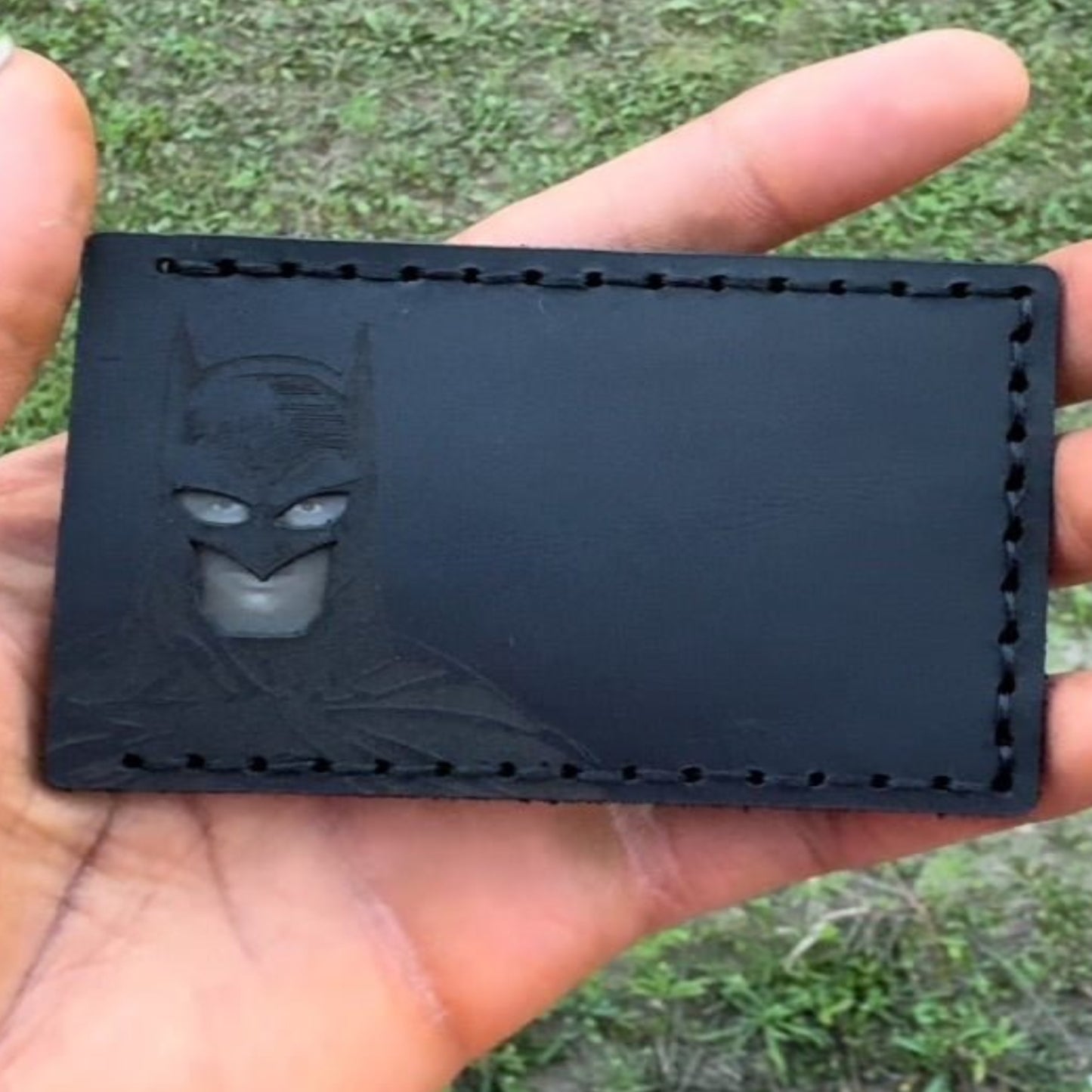Black cardholder with Batman silhouette held in a hand against a grassy background