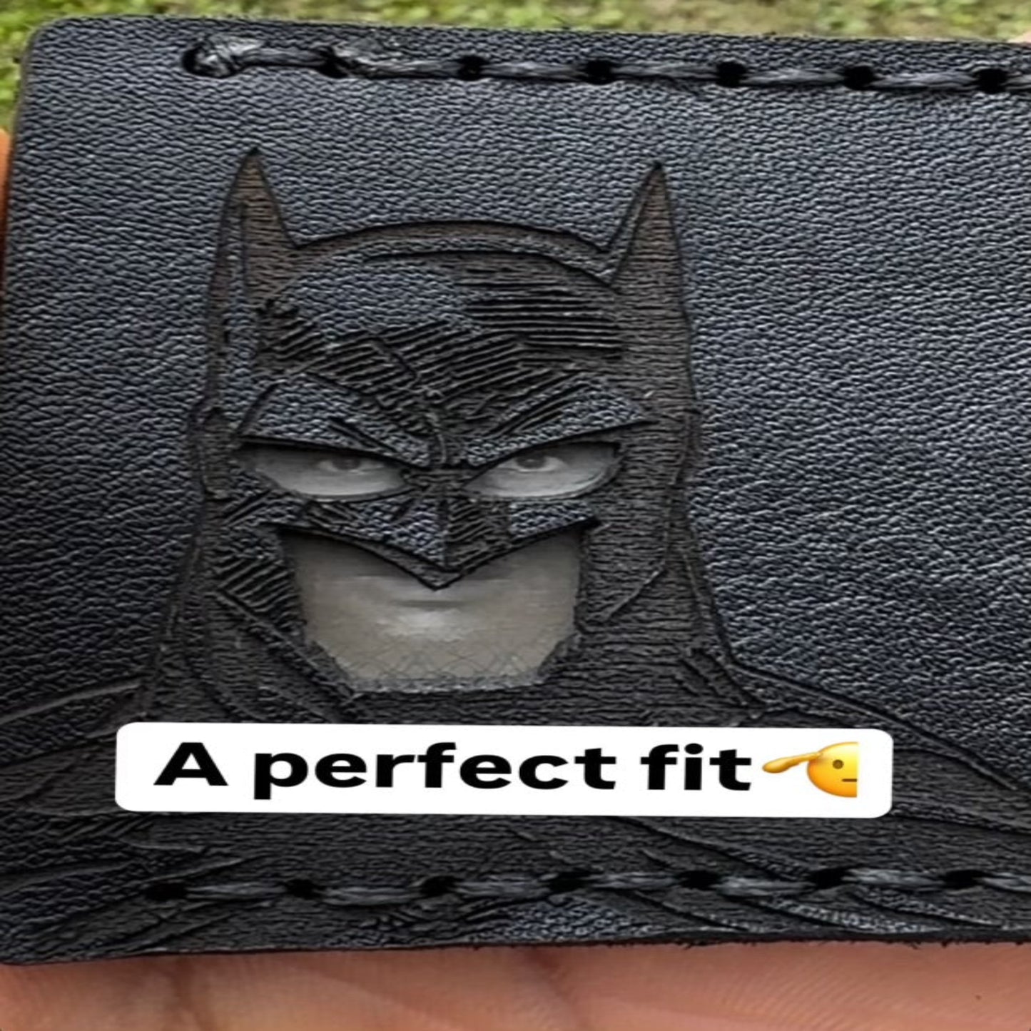 Black leather wallet with Batman emblem and text 'A perfect fit' on a grass background
