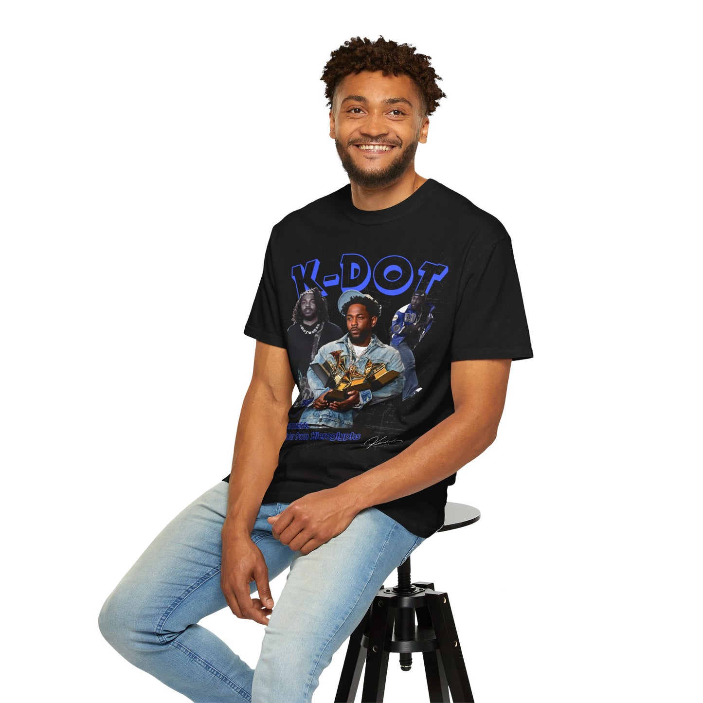 Man wearing a black t-shirt with a graphic design, sitting on a stool against a white background