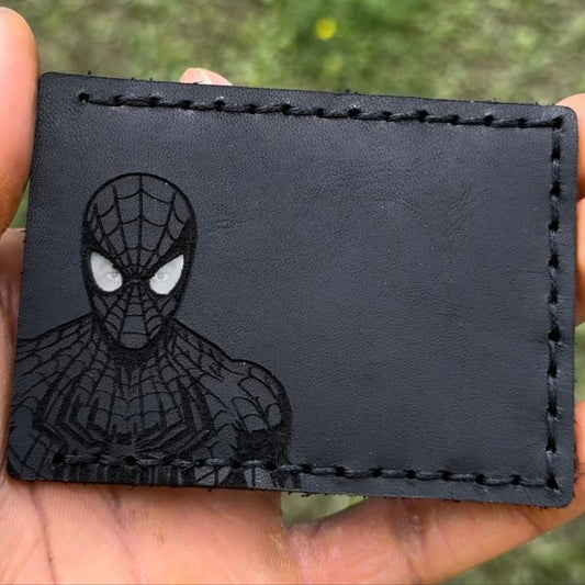Black leather cardholder with Spider-Man design held in a hand against a blurred green background